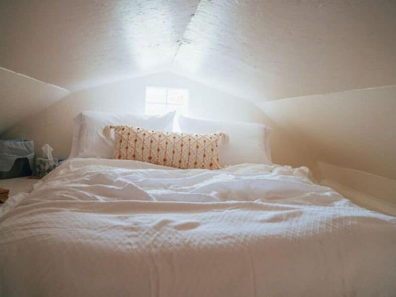 Lofty sleeping area in a Catskills glamping cabin rental, bathed in natural light, with a plush white bed.