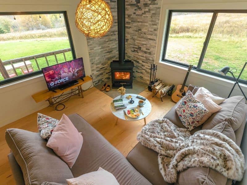 Cozy living room with a modern fireplace, large windows, and comfortable seating in a Catskills rental cabin.
