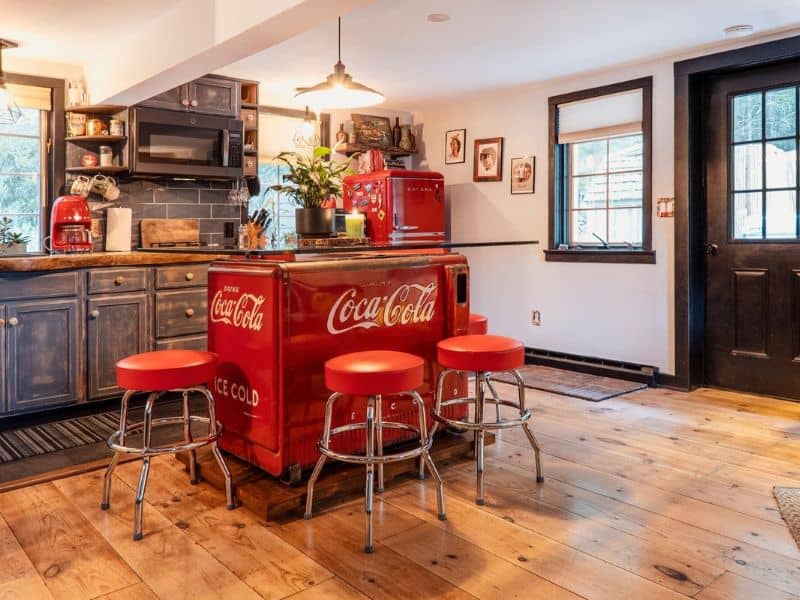 Retro-styled kitchen inside a cozy cabin in the Catskills, featuring a vintage Coca-Cola cooler, red bar stools, and dark wood cabinetry.