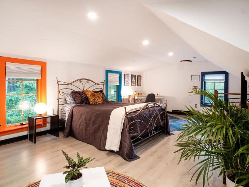 Spacious and bright bedroom in a Catskills rental, with a wrought-iron bed, vibrant orange and blue window frames, and a dedicated workspace.