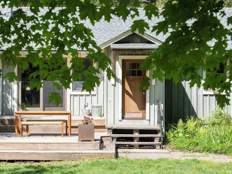 View of a Catskills Vrbo rental cabin exterior with a welcoming front porch, bench, and lush greenery framing the entrance.