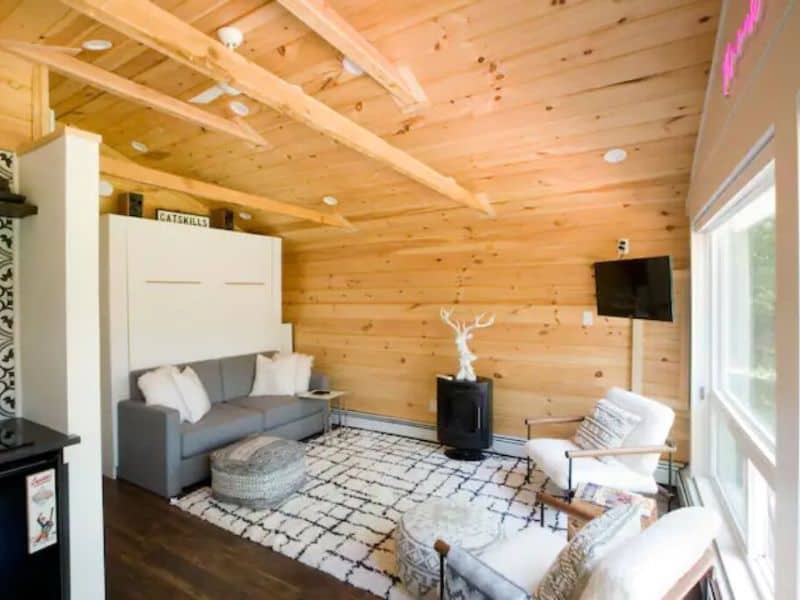 Interior of a Catskills Vrbo rental cabin featuring a minimalist living room with a wooden finish, modern furniture, and a decorative antler piece above a fireplace.