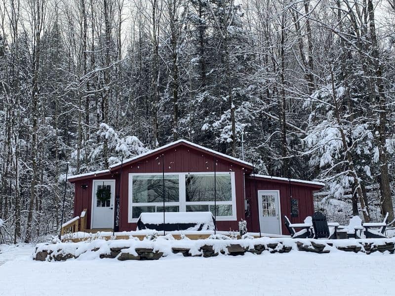 Front view of a cozy cabin in the Catskills adorned with snow, showcasing a red exterior with large windows.