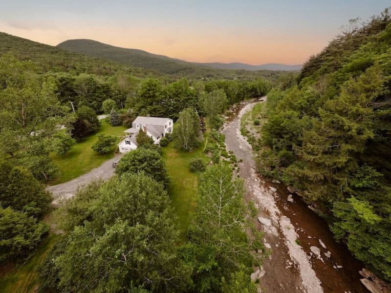 Aerial view of a secluded cozy Catskills cabin surrounded by lush greenery and a meandering stream.