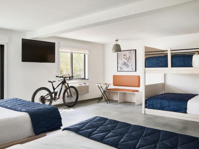 Spacious room at Field Station Joshua Tree with a combination of beds and bunk beds, a bike propped against the wall, and a casual seating area, ideal for groups or families visiting the national park.