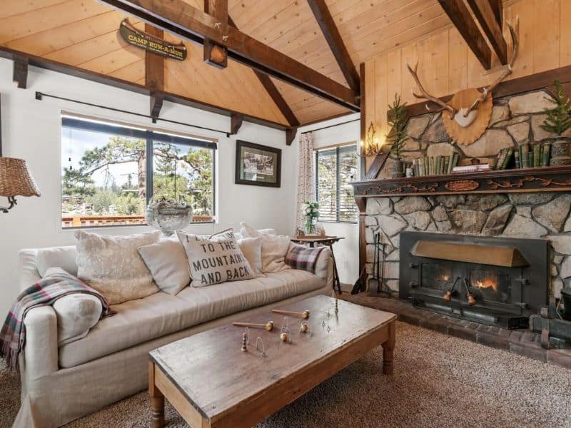 Cozy living room with a stone fireplace and large windows in a Big Bear cabin on the lake, with comfortable furniture and a touch of mountain decor.