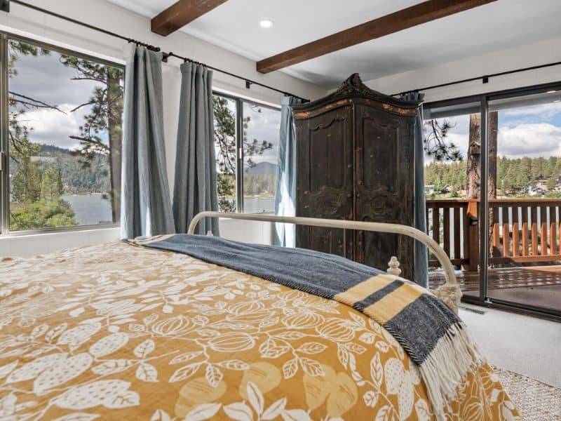 Bright bedroom with a view of Big Bear Lake, showing a bed with a golden yellow bedspread and glass doors leading to a balcony overlooking the water.