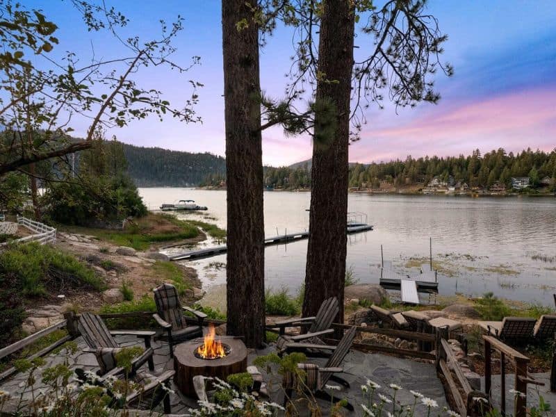Outdoor fire pit area with wooden chairs on a stone patio, offering a lake view of Big Bear Lake CA.