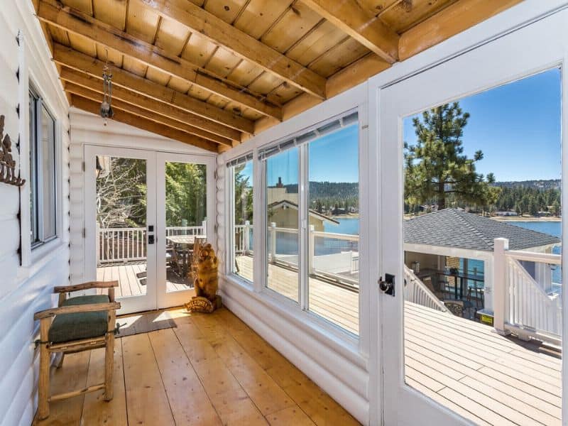 Enclosed sunroom with panoramic windows in a Big Bear rental, offering a bright, airy space with a view of the lake and surrounding trees.