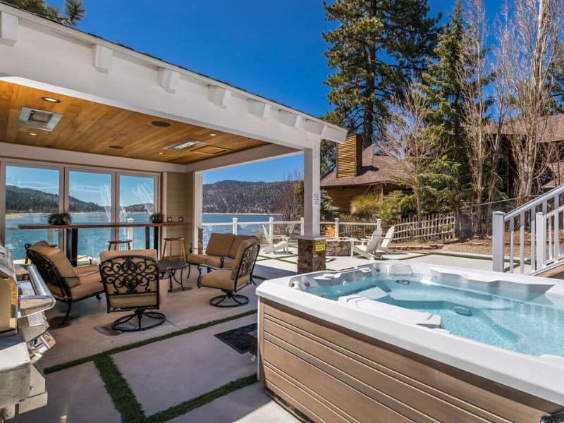 Patio area of a Big Bear cabin on the lake featuring a hot tub, outdoor furniture, and an expansive view of the lake through a covered porch.
