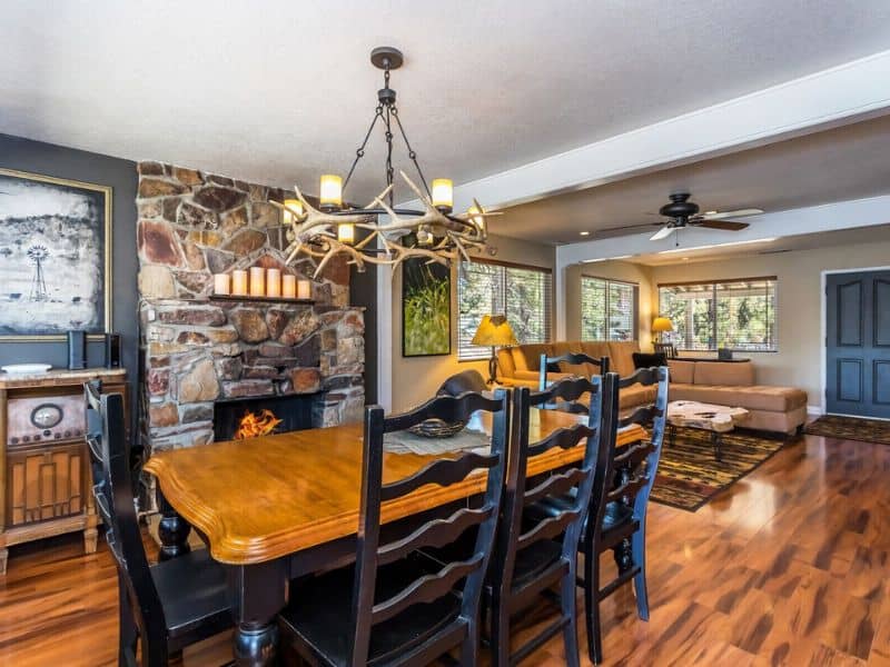 Dining area with a rustic stone fireplace and antler chandelier in a Big Bear Vrbo rental.