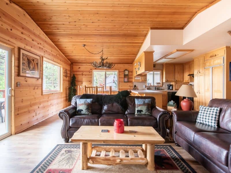 Open-concept living area inside a cabin with leather couches, a wooden coffee table, and an adjoining kitchen, reflecting a cozy cabin atmosphere.