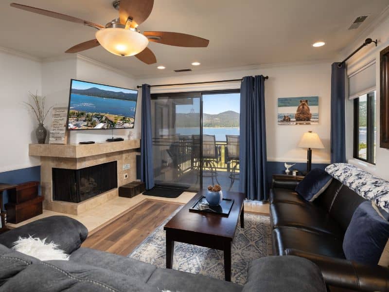 Living room of a lakefront condo in Big Bear with a leather sofa, a fireplace, and sliding doors leading to a balcony with lake views.