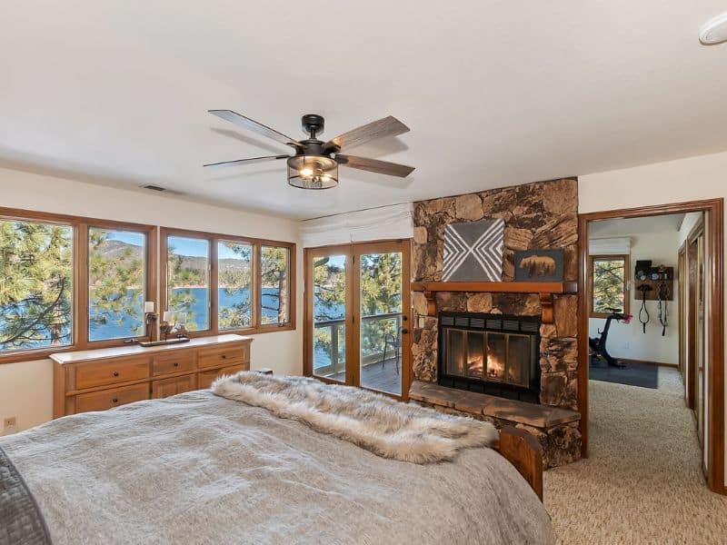 Bedroom with a stone fireplace and lake views in a Big Bear Vrbo cabin, offering direct access to the lakeside balcony.