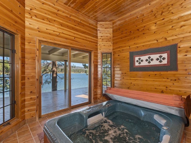 Indoor hot tub room in a lakefront cabin with large windows providing a panoramic view of the lake and surrounding forest in Big Bear.