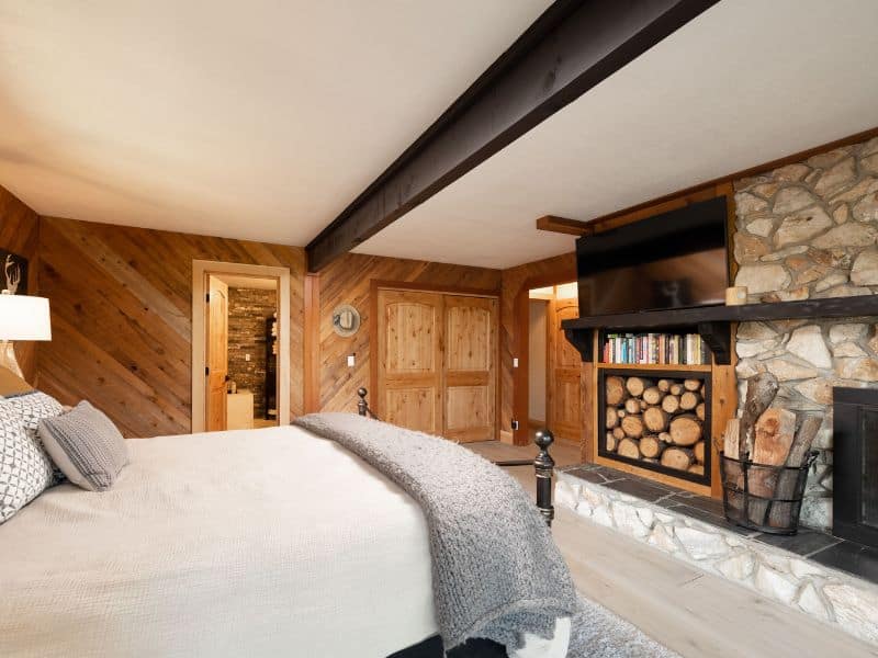 Cozy bedroom inside a luxury cabin with wooden walls, a plush bed, and a stone fireplace, complete with a flat-screen TV.