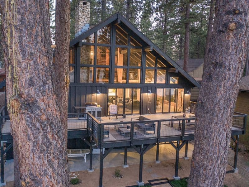 Exterior view of a luxury lakefront cabin in Big Bear with a modern A-frame design with expansive glass windows nestled between pine trees.