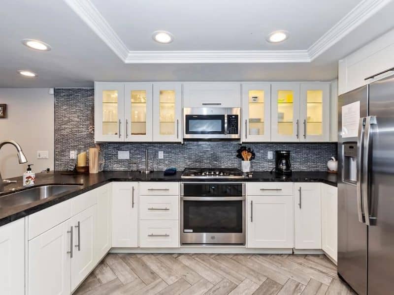 Modern kitchen in a lakefront cabin rental in Big Bear with stainless steel appliances, white cabinets, and a mosaic backsplash.