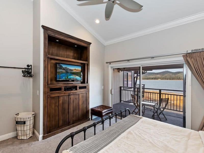 Bedroom in a Big Bear condo rental on the lake, with a large bed facing a built-in television cabinet and glass doors that open to a balcony.