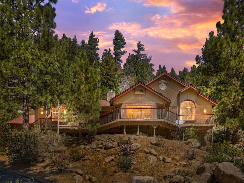 Exterior of a two-story Big Bear cabin on the lake with a spacious deck and large windows, taken during sunset.