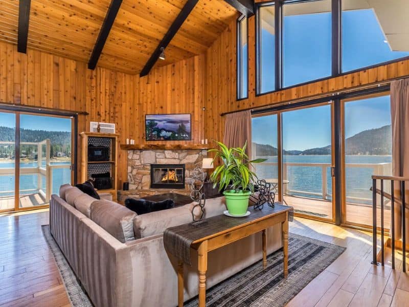 Cozy living space with a stone fireplace and large windows offering panoramic views of the lake in a Big Bear cabin rental.