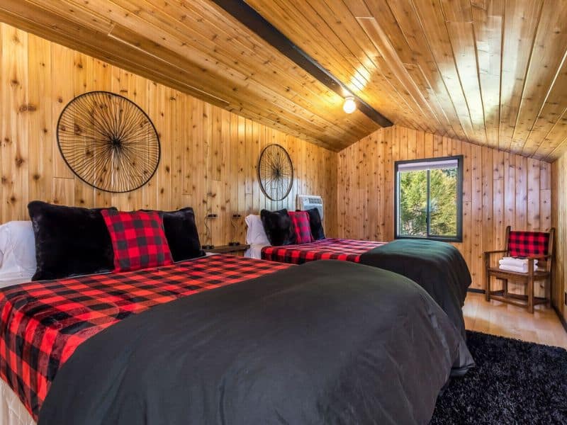 Twin beds with red and black plaid bedding in a wood-paneled bedroom of a lakefront cabin rental in Big Bear.
