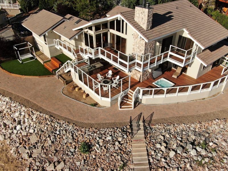 Aerial view of a Big Bear lakefront cabin rental with multiple decks, a hot tub, and a stone pathway leading to the entrance.