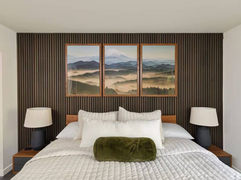 Bedroom in a Mount Rainier cabin featuring a wall-mounted triptych of the mountain landscape above the bed, flanked by chic bedside lamps and minimalist decor.
