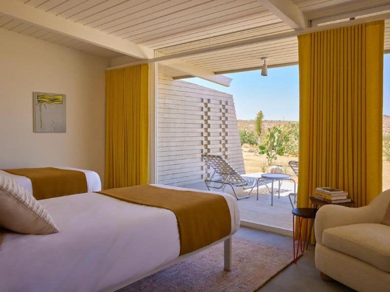 Bedroom within a stylish Joshua Tree Homestead Modern bungalow, seamlessly blending indoor comfort with outdoor tranquility, highlighted by an inviting patio area overlooking the desert expanse.