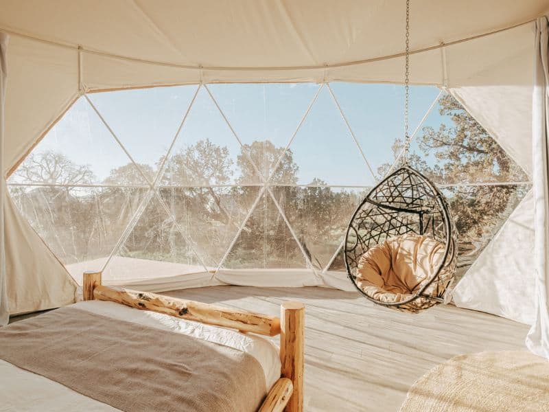 Inside a Clear Sky Resort Grand Canyon dome with a cozy bed and hanging swing chair, surrounded by transparent walls that connect guests with nature.