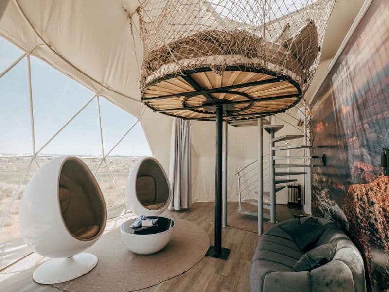 Futuristic interior of a Clear Sky Resorts dome with egg chairs and a loft net bed, for guests seeking a luxury glamping experience near the Grand Canyon South Rim.