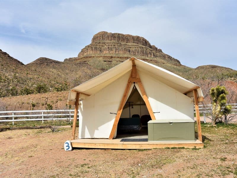 Canvas glamping tent with bed and storage chest at Grand Canyon Western Ranch, against a backdrop of desert mountains.
