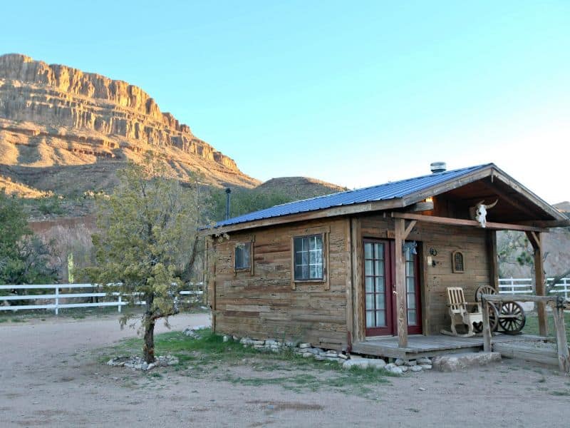 Rustic wooden cabin with front porch at Grand Canyon Western Ranch in a desert landscape at sunset.