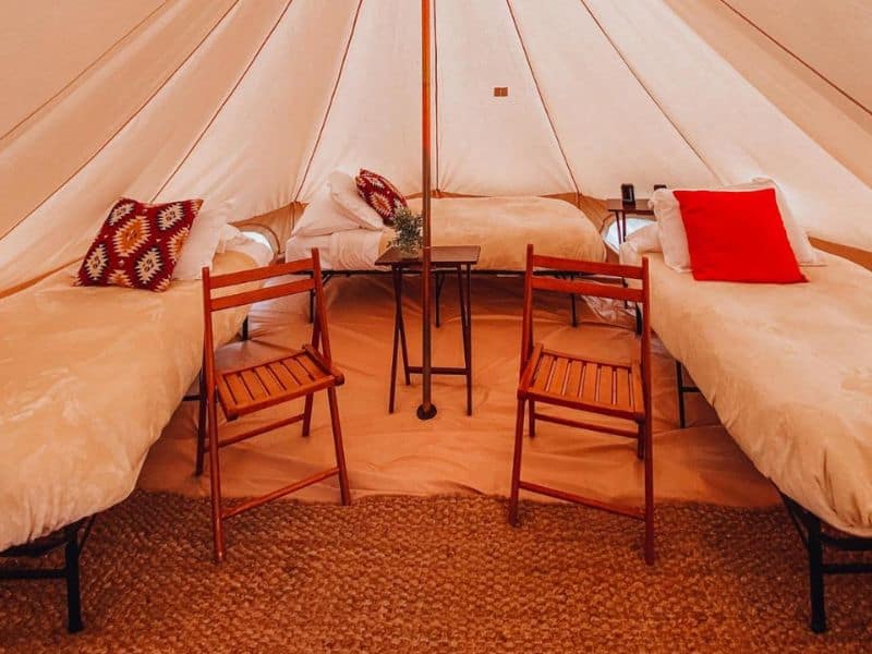Twin beds with red pillows and rustic wooden chairs inside a Wander Camp tent, set up for a comfortable stay while glamping near the Grand Canyon.