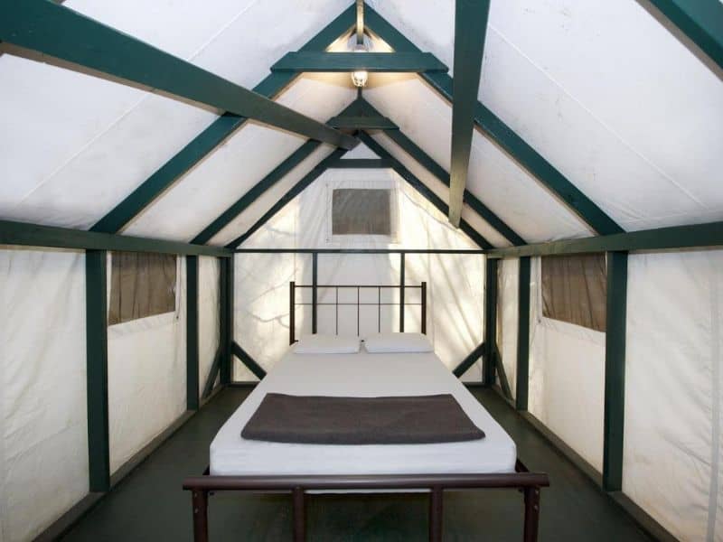 Inside view of a basic Yosemite Valley glamping tent in Curry Village with a neatly made bed and sturdy wooden frame.