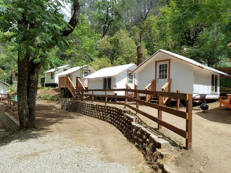 Canvas tent cabins on wooden platforms line a gravel path in a shaded grove at Indian Flat Campground, offering basic glamping near Yosemite.