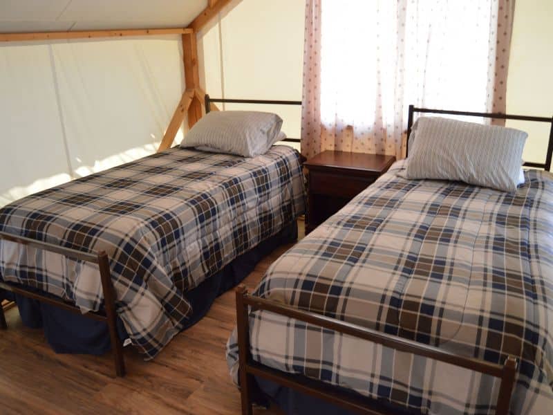 Two single beds with plaid bedding in a well-lit tent cabin at Indian Flat Campground near Yosemite.