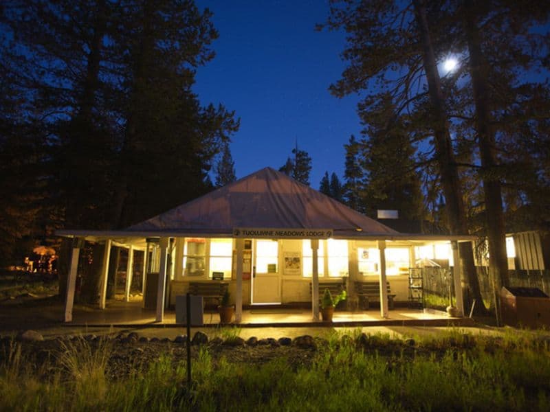 Night view of Tuolumne Meadows Lodge in Yosemite with lit windows against the dark forest backdrop.