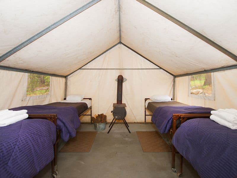 Interior of a canvas tent cabin at Tuolumne Meadows Lodge with twin beds and a central wood stove, offering a rustic glamping experience in Yosemite.