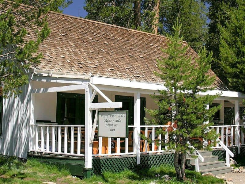 A white-painted cabin with a shingled roof and a wooden porch at White Wolf Lodge, surrounded by pine trees.