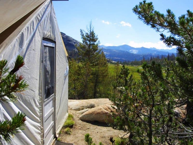 View from the entrance of a canvas tent at a Yosemite High Sierra Camp site, overlooking a scenic valley with pine trees.