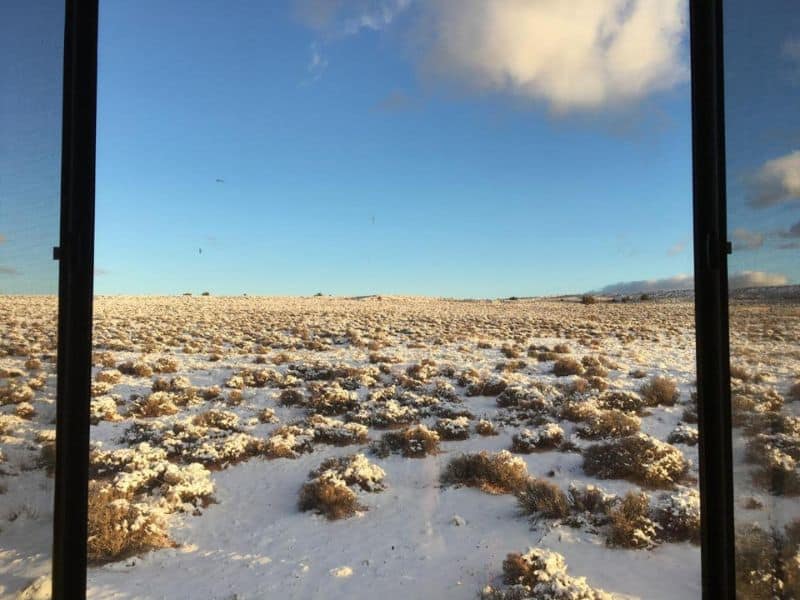 View from a Kyo͞ob at Shash Dine' Eco Retreat showing a snow-dusted desert terrain near the Grand Canyon through a large window.