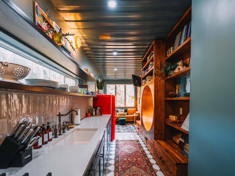 Interior of The Roca Box Hop's kitchen area, showcasing the creative use of space in a Hocking Hills container home, with a long counter, shelving, and a peek into the cozy lounge.