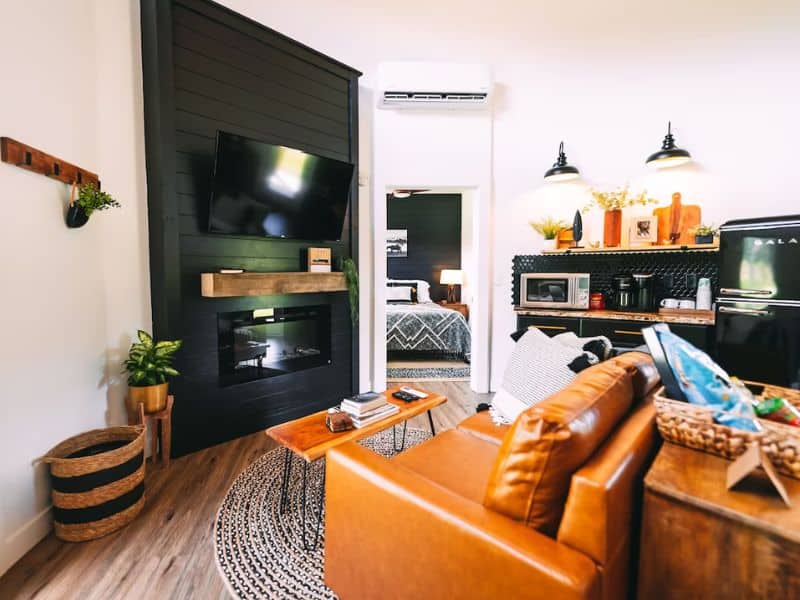 Cozy living space inside The Silo, a unique Hocking Hills grain silo container home, featuring a leather couch, wall-mounted fireplace, and TV.