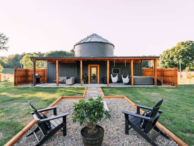 Exterior view of The Silo Tiny House with a distinctive circular design, patio area with hanging chairs, in Ohio's Hocking Hills.