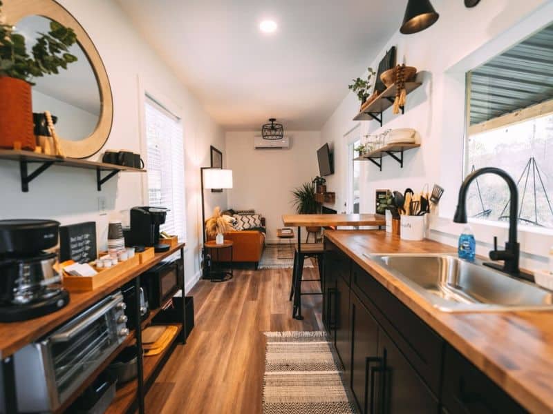 Modern kitchen inside a Hocking Hills container cabin with stainless steel appliances, wooden countertops, and a cozy living area in the background.