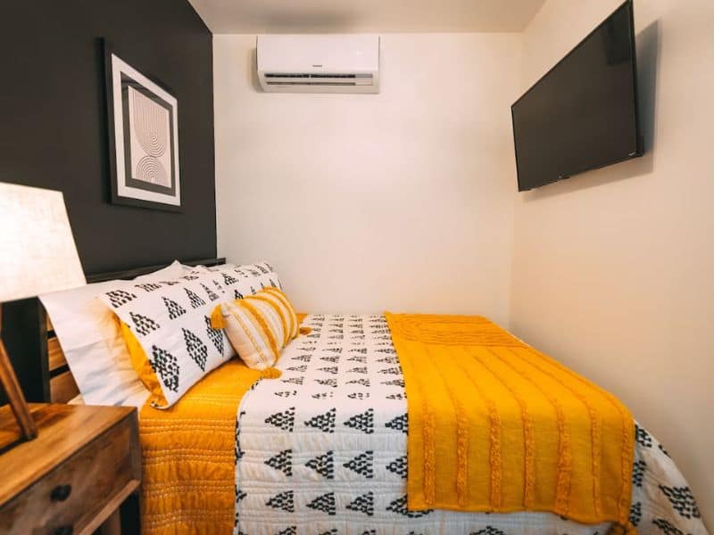 Compact bedroom in a Hocking Hills shipping container cabin featuring a black and white geometric bedding set with a mustard throw and wall-mounted TV.