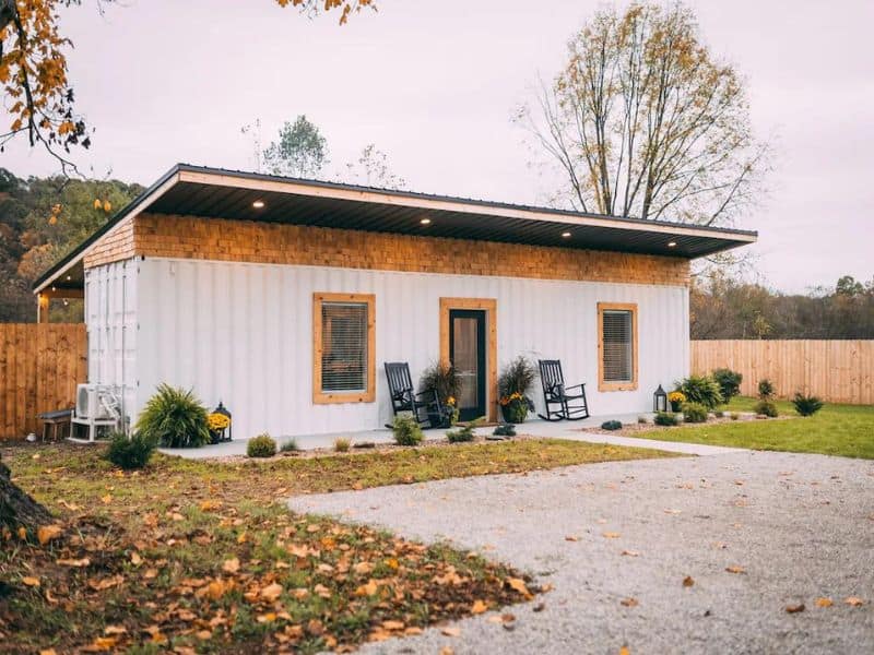 Exterior view of Luna Cottage, a minimalist Hocking Hills container cabin, with wood accents and a welcoming porch with rocking chairs.