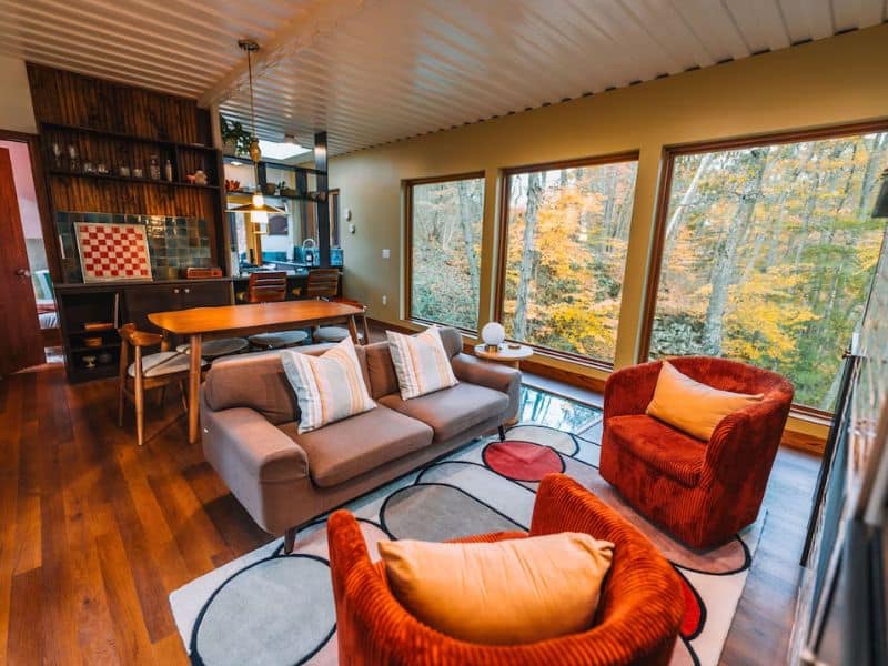 Inviting mid-century style living room in The Ellwood with plush seating and expansive windows offering a forest view. Hocking Hills container cabin.