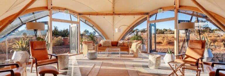 Interior view of the communal glamping tent and reception at Under Canvas Grand Canyon with arched canvas roof and panoramic windows, furnished with leather chairs and wood accents.